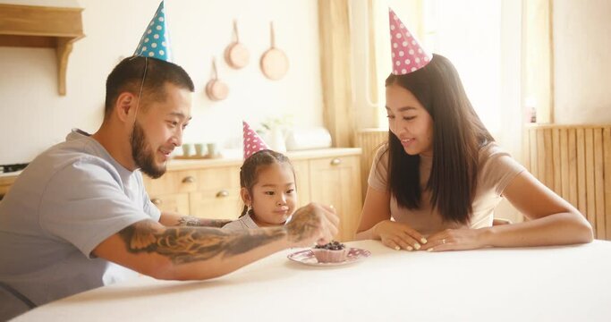 Asian kid celebrates birthday with parents and blows candle