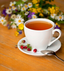 cup of aromatic tea, wild strawberry, bouquet of wild flowers on a wooden background