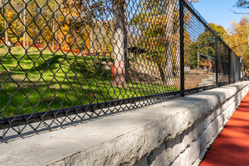 Interesting green and red outdoor basketball court at school playground.  Court includes retaining walls and black vinyl coated chain link fence.	