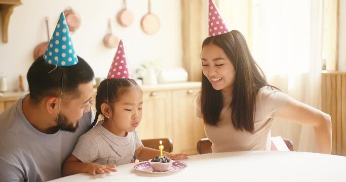 Asian kid celebrates birthday with parents and blows candle