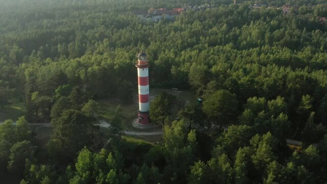 Close flyby of the lighthouse on the hill, lighthouse is located in the middle of forest on highest hill point, Baltic sea can be seen