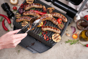 Grilled sausages and vegetables on electric grill at domestic kitchen