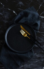 Empty black plate, fork ,knife, linen napkin top view . Black kitchen utensils set on black marble ...