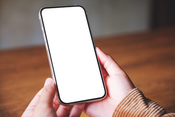 Mockup image of a woman holding mobile phone with blank desktop screen in cafe