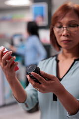 Female client being indecisive about medicaments, looking at box of cardiology drugs and bottle of sleeping pills. Woman examining packages of supplements at pharmacy shop. Close up.