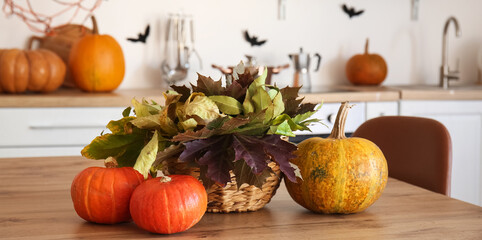Obraz na płótnie Canvas Basket with autumn leaves and Halloween pumpkins on dining table in kitchen