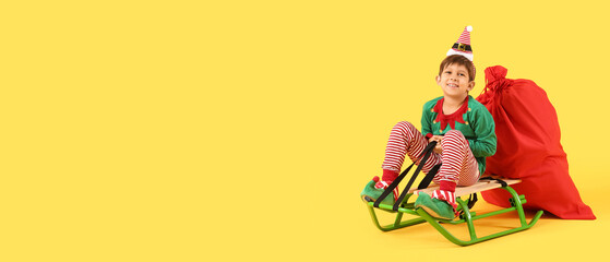 Cute little elf with Santa bag sitting on sledge against yellow background with space for text