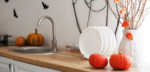 Fresh pumpkins, plates and vase with tree branches on counter in kitchen
