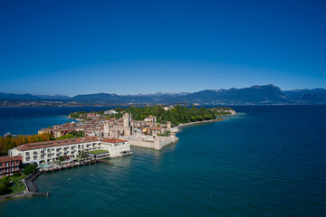 Naklejka na ściany i meble Top view of the town of Sirmione, Italy. Lake Garda, a tourist destination in northern Italy. Autumn in Italy on Lake Garda, Sirmione peninsula. Trees in the autumn season.