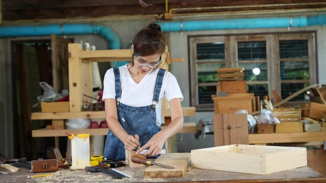 portrait of beautiful asian woman carpenter dealing with handicraft, woman has own business connected with making wooden furniture in workshop ,cinema tone