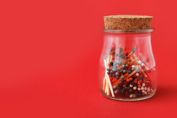 Glass jar with different colorful matches on red background