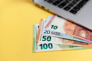 Different Euro bills on a laptop background and on a yellow background, Purchases and earnings via the Internet. Cash paper currency, payment, earnings and savings, the concept of money and finance.