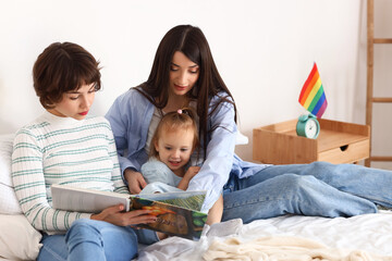 Lesbian couple reading story to their little daughter in bedroom