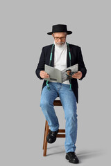 Mature fashion designer reading magazine on grey background