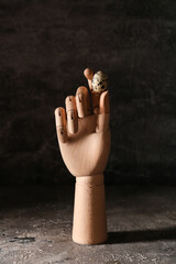 Wooden hand with quail egg on dark background