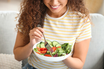 Young African-American woman eating healthy salad at home. Diet concept