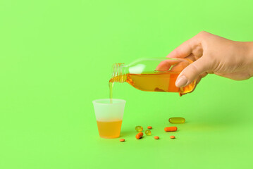 Woman pouring cough syrup from bottle into cup on green background