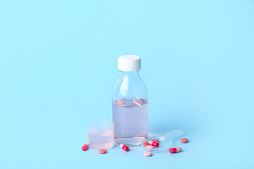 Bottle of cough syrup, cup, spoon and pills on blue background