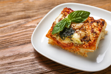 Plate with tasty Italian pie with mozzarella and pesto sauce on wooden background, closeup