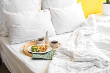 Tray with delicious breakfast and cups of coffee on comfortable bed