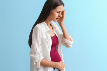 Young pregnant woman with nosebleed on blue background