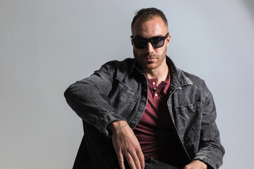 Fototapeta premium seated young guy with sunglasses holding elbow on knee and posing