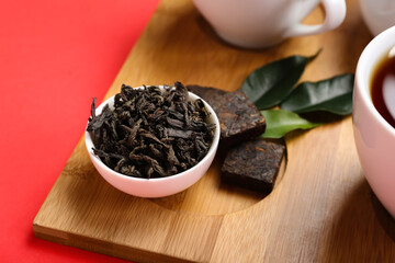 Board with bowl of dry puer tea on red background, closeup