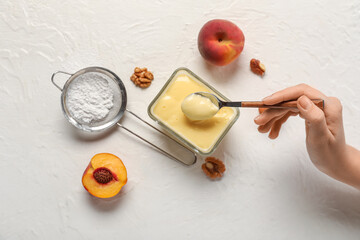 Female hand with bowl of tasty vanilla pudding, sugar powder and peaches on light background