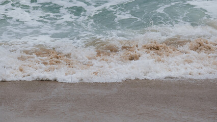 View of ocean waves and sand on the beach of tropical seas in Thailand. Strong sea waves crash to shore in the rainy season.