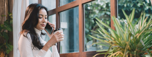 young businesswoman talking on the phone about the success of the business. Woman talking on the phone and smiling near the window at the cafe.