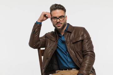 man with elbow on chair adjusting glasses and posing in a cool way