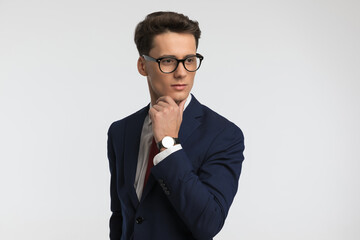 pensive man with glasses thinking and looking to side while touching chin
