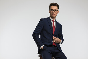 Obraz na płótnie Canvas confident businessman with glasses closing suit and posing with hand in pocket