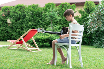 Cute boy sitting on the chair and playing on guitar on the backyard