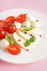 Plate with tasty mozzarella cheese, tomatoes and basil on pink background