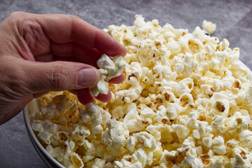 Female hand holds popcorn on grey concrete background.