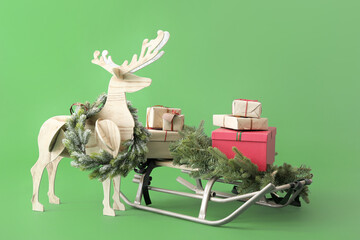 Wooden reindeer with Christmas wreath, sledge and presents on green background
