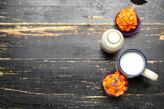 Tasty Halloween cupcakes, bottle and cup of milk on wooden background