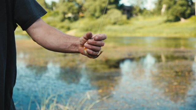 Slow motion, close-up of male fisherman hand catching and holding freshly caught flapping live fish on fishing hook. Concept of man hobby angling. Countryside landscape, wild river in summer day.