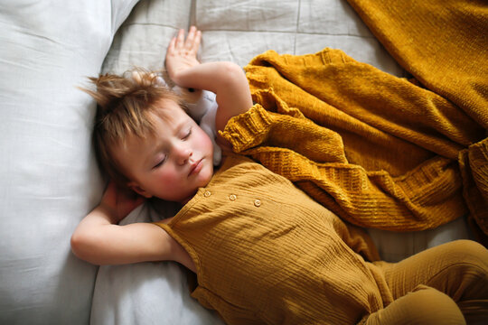 Cute Sleeping Toddler Child In Yellow Jumpsuit On Bed, Top View.