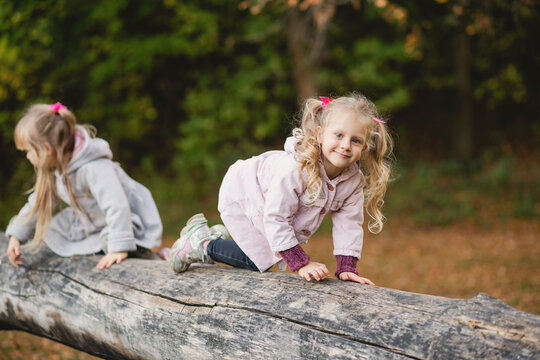 Two cute children climb, balance on a fallen log in an park.