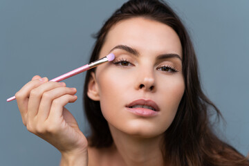 Close-up beauty portrait of woman with perfect skin and natural makeup, full nude lips, holding a bright pink eyeshadow brush, cosmetic concept