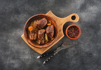 Stewed pork cheeks with vegetables on wooden board with pepper. - obrazy, fototapety, plakaty