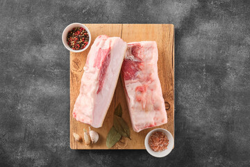 Two pieces of raw pork lard with spices on wooden board, top view