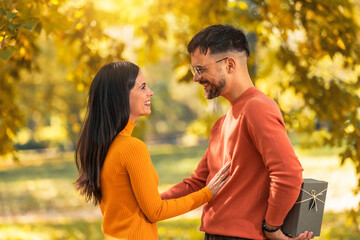 Fototapeta premium Caucasian boyfriend give box gift to lovely pretty girlfriend in autumn park surprise present for valentine's day birthday anniversary symbol of love affection