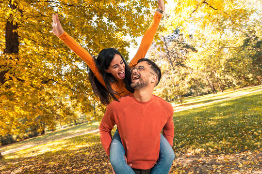 Smiling couple having fun in autumn park. Boyfriend carrying his girlfriend on piggyback