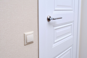 A white door in the home room and a light switch. Metal door handle and plastic light switch