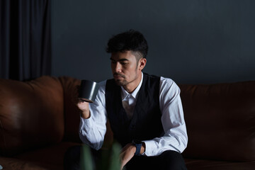 Portrait of a good looking and discreet Asian man sitting on the sofa drinking coffee