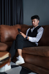 Portrait of a good looking and discreet Asian man sitting on the sofa playing on the phone