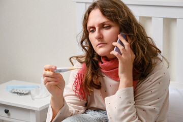 Sick woman calls the doctor on the phone with a thermometer in her hand, fever. Adult ill woman...